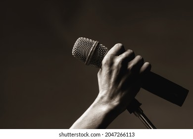 Man's hand holding a wireless microphone on a stand.