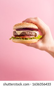 Man's hand holds burger on pink background, menu for cafe, fastfood