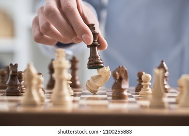 Man's hand holds a chess piece king. A dark colored chess piece. The figure flies. Chess game making a move by a player is an intellectual game.
 - Shutterstock ID 2100255883