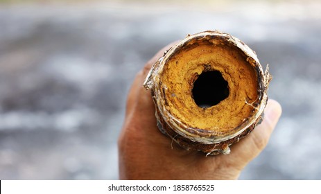 Man's hand holds a clogged metal pipe. Old water pipes had rusty slag and clogged dirt inside the pipe. On the background of a cement floor with a copy area. Close focus and select an object
