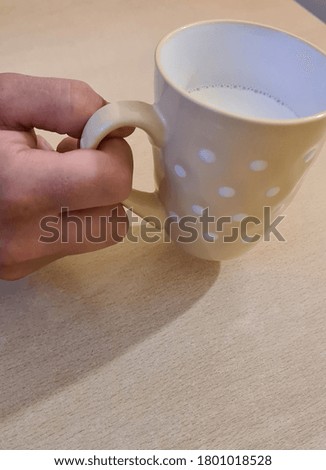a man's hand holds a cup of warm white milk.