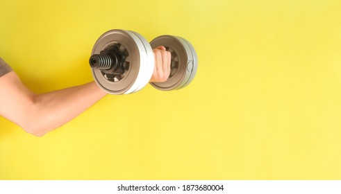 A Man's Hand Holds A Dumbbell. Classes At Home, Sunny Color. Bright Yellow Background.