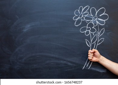 A man's hand holds flowers drawn on a chalkboard in his hand.