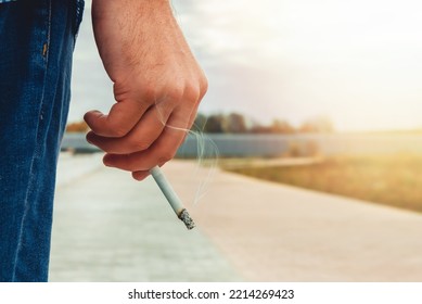 The man's hand holds a lit cigarette. Cigarettes are harmful to health