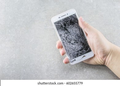Man's hand holds mobile phone with broken touchscreen on gray background.