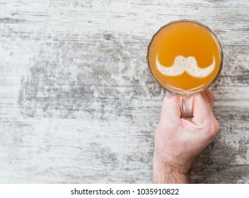 Man's Hand Holds A Mug Of Beer With Silhouettes Of Mustache On A Beer Foam. Top View. Space For Text