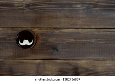 Man's Hand Holds A Mug Of Beer With Silhouettes Of Mustache On A Beer Foam. Top View. Space For Text