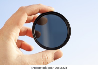 Man's Hand Holds A ND (neutral Density) Optical Filter Against Sky