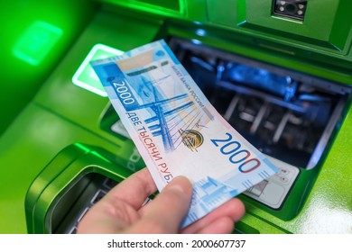 Man's hand holds new Russian banknote of two thousand rubles against background of green cash machine - Shutterstock ID 2000607737