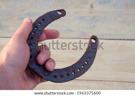 A man's hand holds an old horseshoe. Natural wood background. Place for your text.