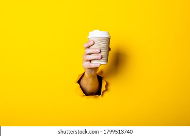 Man's hand holds a paper cup with coffee closed by a bump on a bright yellow background - Powered by Shutterstock