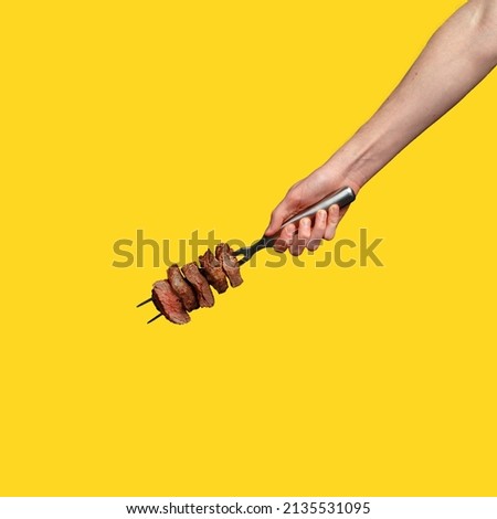 a man's hand holds pieces of roasted meat on a fork.