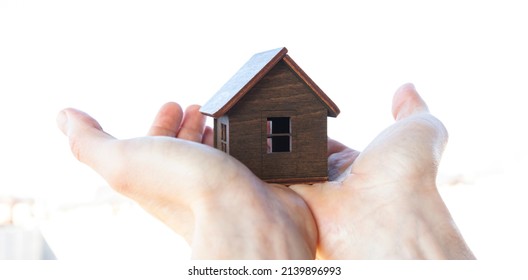 Man's hand holds wooden house against the sky