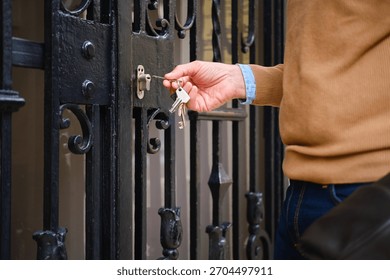 Man's hand inserting a key into an ornate black iron gate lock, entering home
