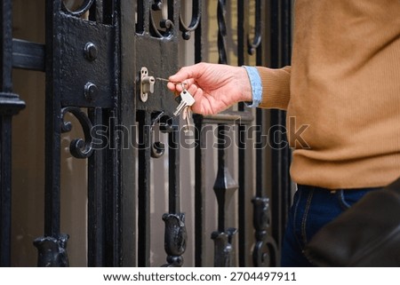 Man's hand inserting a key into an ornate black iron gate lock, entering home