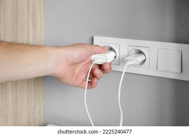 A man's hand inserts a charger plug, wires into a socket near the bed - Shutterstock ID 2225240477
