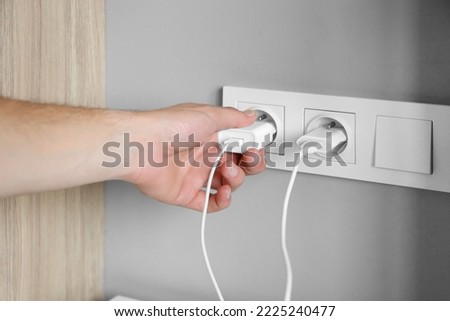 A man's hand inserts a charger plug, wires into a socket near the bed