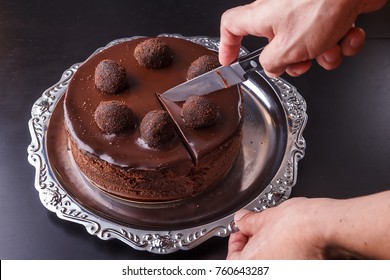 A Man's Hand With A Kitchen Knife Above A Chocolate Homemade Biscuit Cake On A Metal Plate