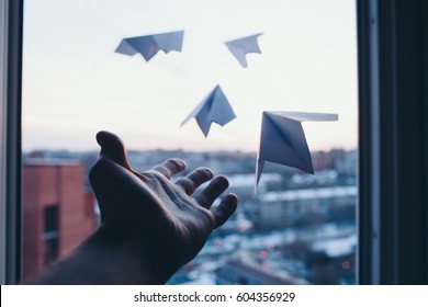 Мужская рука отпускает маленькие бумажные самолетики из окна в никуда