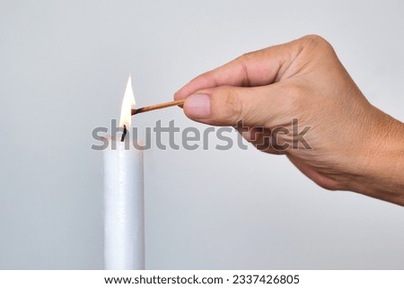 A man's hand lights a white candle with a matchstick 