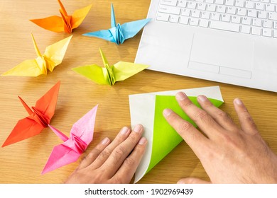 A Man's Hand Looking At A Computer And Making Origami