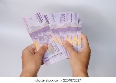 A Man's Hand Is Making A Payment. Female Hand Showing Indonesian Rupiah Note. Indonesian Rupiah The Official Currency Of Indonesia. Uang 10000 Rupiah Bank Indonesia