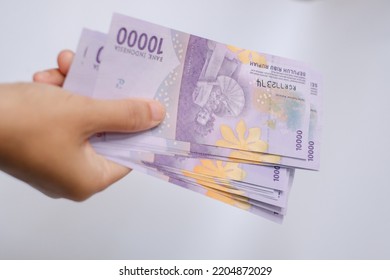 A Man's Hand Is Making A Payment. Female Hand Showing Indonesian Rupiah Note. Indonesian Rupiah The Official Currency Of Indonesia. Uang 10000 Rupiah Bank Indonesia