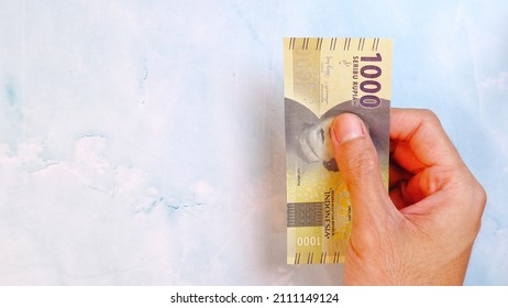 A man's hand is making a payment. Indonesian Rupiah the official currency of Indonesia.  Male hand showing Indonesian Rupiah note. Business and finance concept. Uang 1000 Rupiah. Bank Indonesia - Shutterstock ID 2111149124