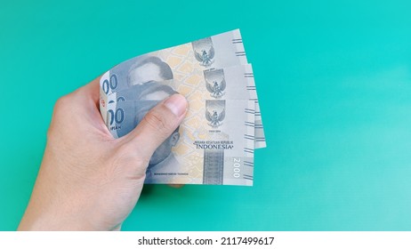 A man's hand is making a payment. Indonesian Rupiah the official currency of Indonesia.  Male hand showing Indonesian Rupiah note. Business and finance concept. Uang 2000 Rupiah. Bank Indonesia - Shutterstock ID 2117499617