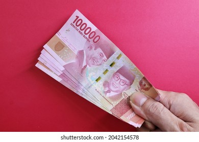 a man's hand is making a payment. Male hand showing Indonesian rupiah note. Indonesian Rupiah the official currency of Indonesia. Business concept, Red Background. Uang 100000 Rupiah Bank Indonesia