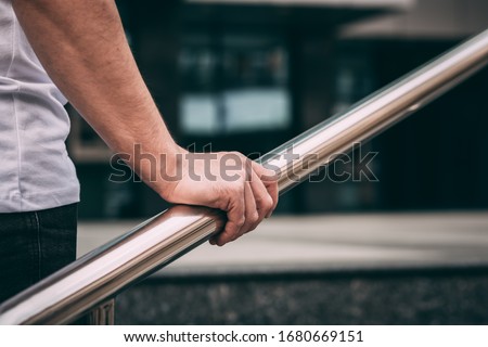 man's hand on the railing, a man in a white T-shirt and black jeans. go upstairs. outside