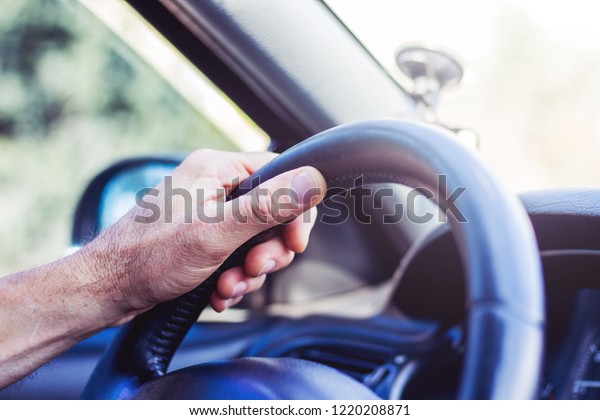 Man\'s hand on steering wheel of a car. Driving on\
the road