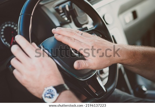 A man\'s hand on the steering wheel honks while\
standing in traffic