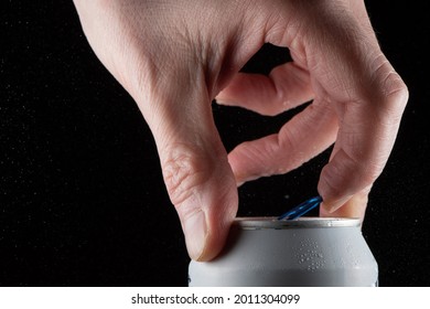 A man's hand opening a soda can on a black background and showing the splash when opening the can.