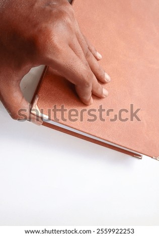 A man's hand opens a brown leather-bound book. Opening the book from the corner