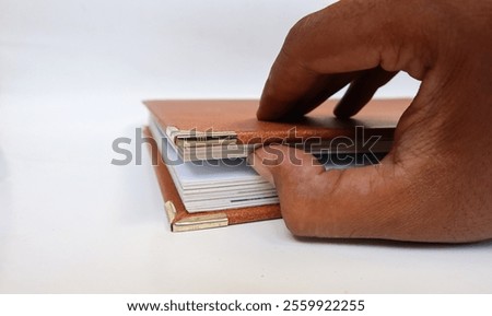 A man's hand opens a brown leather-bound book. Opening the book from the corner