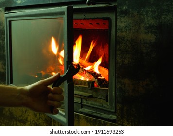 A man's hand opens the glass door of the fireplace in which the wood is burning. Modern closed fireplace with glass.