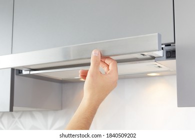 Man's hand opens kitchen hood for cooking or replacing filter. Modern interior on background.