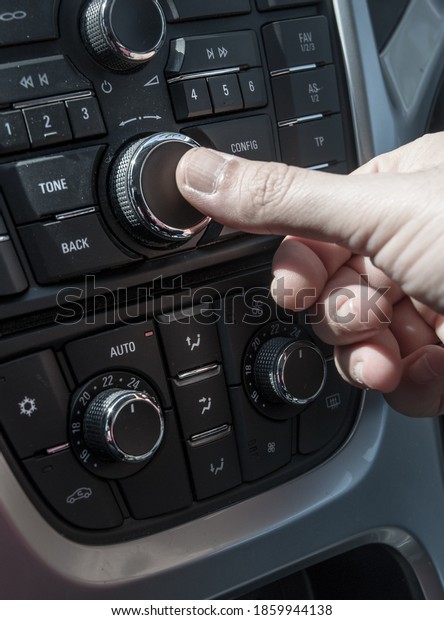 Man\'s\
hand operates the controls of the stereo of a modern car with\
automatic climate control and temperature\
control\
