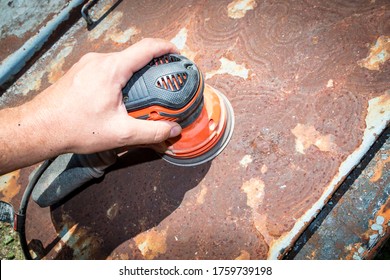 Man's hand operates a disc/orbital sander, to remove paint and rust from metal doors