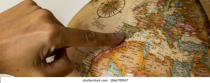 A man's hand is pointing, on a beautiful and vintage map of a ball of the world, Spain, a country in Europe, which is part of the European Union. Its capital is Madrid