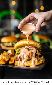 A Man's Hand Pouring Sauce On The Appetizing Burger