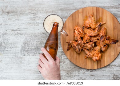 A Man's Hand Pours Beer From A Bottle Into A Mug Near Fried Chicken Wings. Top View