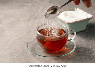 A man's hand pours a teaspoon of sugar into a cup of tea. - Powered by Shutterstock