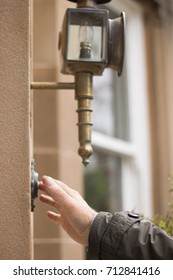 Man's Hand Presses A Doorbell Button On A Wall Of A House. It's Morning Or Day. A Bronze Night Lamp Does Not Light. Concept: Guests On A Threshold.