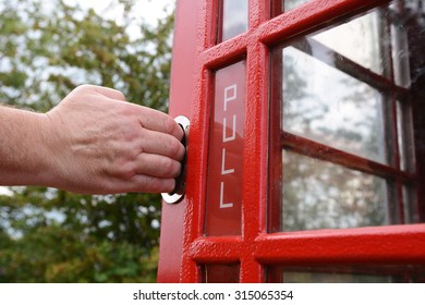 Man's hand pulling open red door of an old-fashioned British telephone box