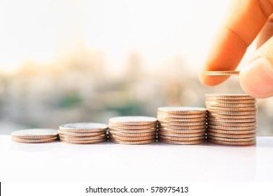 Die Hand des Menschen steckte Geldmünzen in den Stapel von Münzen. Geld, Finanzen, Geschäftswachstum Konzept.