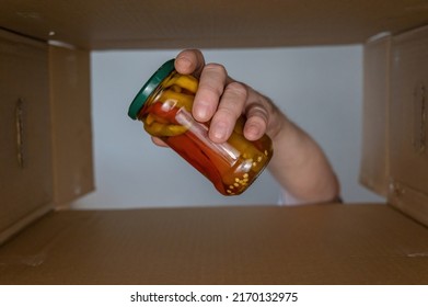 A Man's Hand Puts Food In A Cardboard Box. Canned Vegetables Are Put In A Donation Box. A Glass Jar Of Hot Peppers. Bottom View. Inside View. Close-up. Selective Focus.