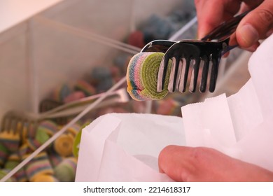 A Man's Hand Puts A Striped Candy In A Paper Bag In A Candy Store.