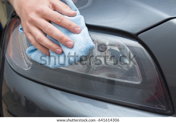 Man\'s hand with rag cleaning a dirty car lamp in\
the garage. Early spring washing or regular wash up. Professional\
car wash by hands.